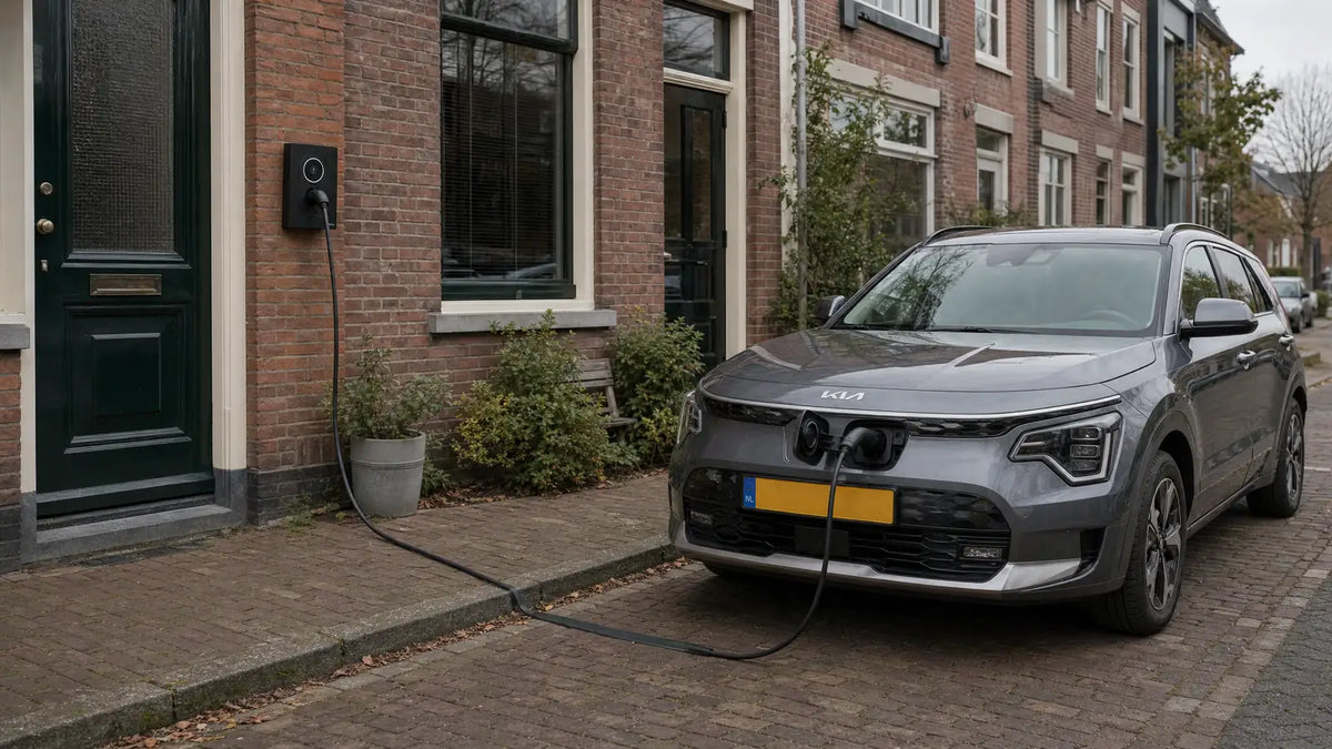 Laadkabel die afgedekt over de stoep loopt naar een elektrische auto aan de straat