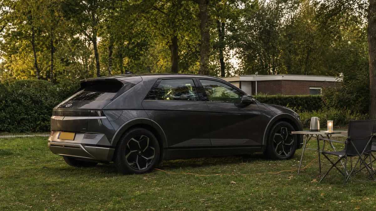 Elektrische auto op een camping met een waterkoker en lamp op een tafeltje ernaast