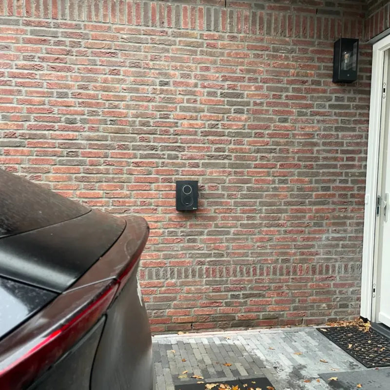 Zaptec Go laadpaal aan een bakstenen gevel bij de voordeur, met een elektrische auto op de oprit
