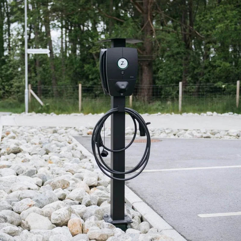 Zaptec Pro laadpaal op een zwarte paal met afdak en opgerolde laadkabel, naast een parkeervak met witte stenen.