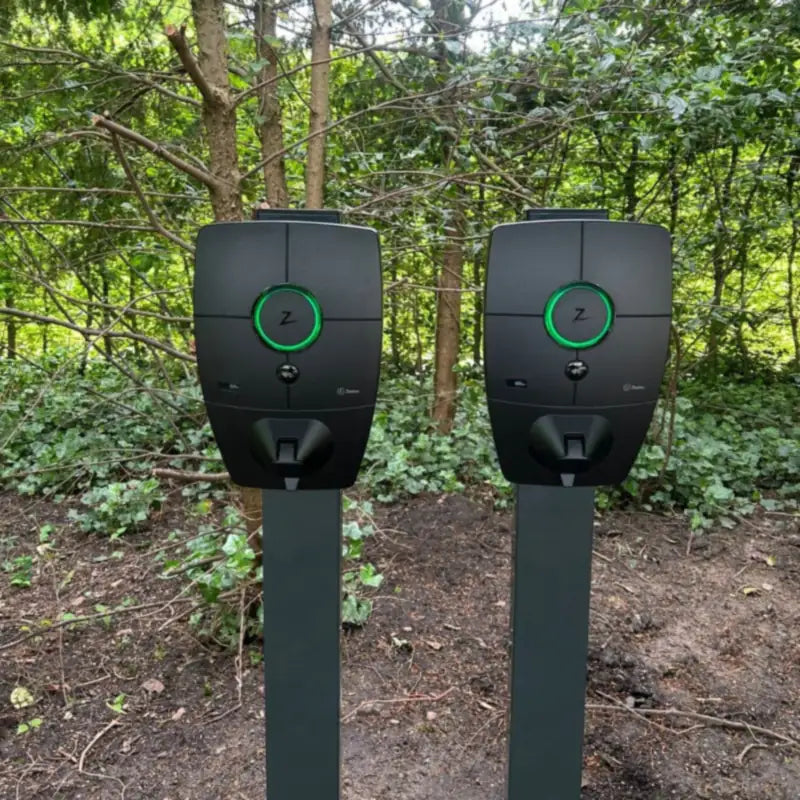 Twee Zaptec Pro laadpalen naast elkaar op donkergrijze palen, met groen oplichtende statusring voor een groene haag.
